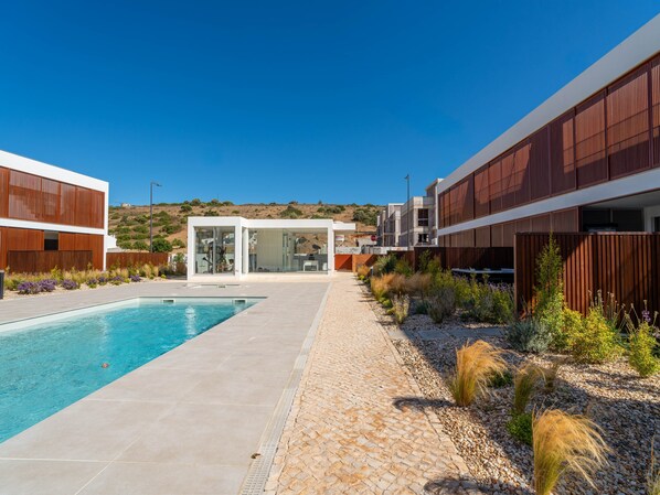 A modern pool area with a clear blue pool, a paved walkway, and a building with large windows and a glass door.
