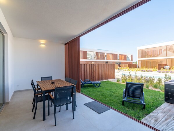 A modern patio with a table and chairs, a grassy area, and a view of a contemporary building. - Magnolia – Your Holiday Retreat in Burgau (Luz)