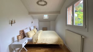 Una camera da letto con un letto, una scrivania, un termosifone, una finestra vista verde e una lampada a soffitto.