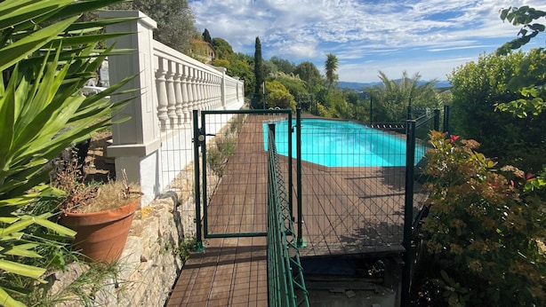 Una piscina circondata da verde e un cielo sereno, con una recinzione bianca.