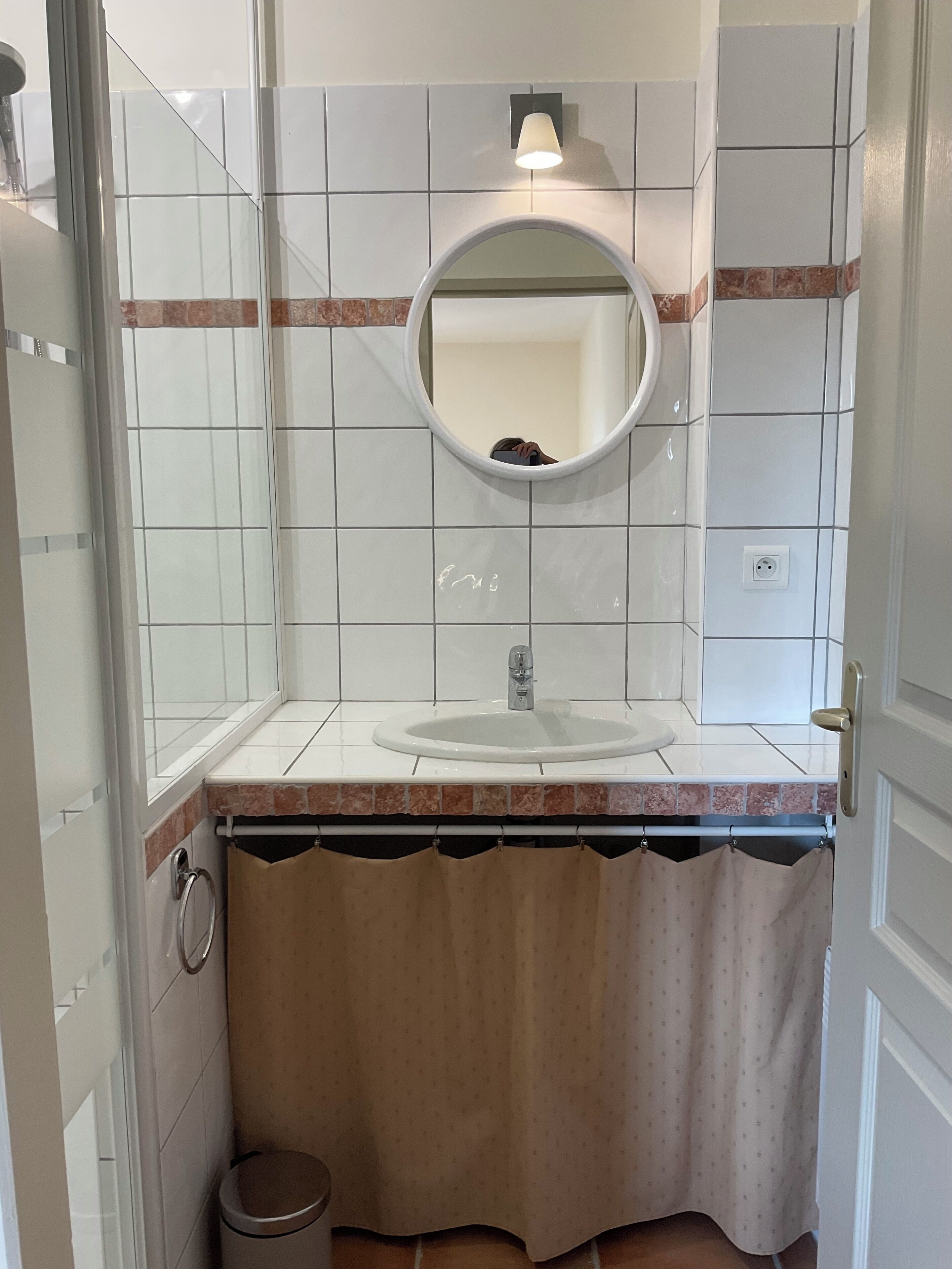 A bathroom with a white sink, a mirror, a towel rack, and a trash bin.