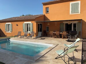 Ein Haus mit Swimmingpool, Sitzgelegenheiten im Freien und einer Grillanlage.