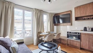 A compact living space with a dining area, kitchenette, and a large window with curtains. - SITUATED IN A LIVELY AND AUTHENTIC PARISIAN NEIGHBORHOOD – LE MARAIS (Paris)