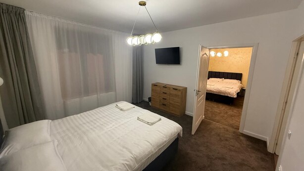 A bedroom with a bed, a dresser, a TV, and a door leading to another room. - Spacious 2-Room Apartment near Brașov Center | Random Studio | Pet frendly (Brașov)