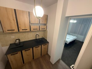 A compact kitchen with wooden cabinets, a black countertop, and a modern pendant light. - Spacious 2-Room Apartment near Brașov Center | Random Studio | Pet frendly (Brașov)