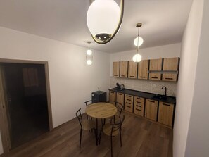A compact kitchen with wooden cabinets, a round dining table, and pendant lighting. - Spacious 2-Room Apartment near Brașov Center | Random Studio | Pet frendly (Brașov)