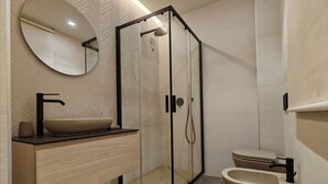 A modern bathroom with a glass-enclosed shower, a round mirror, a beige sink, and a toilet. - Modern and cozy suite for couples and families "Calliope" (Vernazzano Basso)