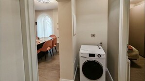 A laundry room with a front-loading washing machine, a dining area with a table and chairs, and a hallway leading to another room. - Modern and cozy suite for couples and families "Calliope" (Vernazzano Basso)