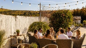 An outdoor patio with wicker furniture, a round glass table, and string lights. - Dragonfly Retreat Málaga | Private Villa & Rose Pool (Coín)