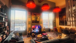 A living room with a television, a bookshelf, a sofa, and large windows with a city view. - Exceptional duplex loft on Marseille's Old Port - Panoramic view (Marseille)
