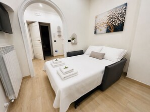Ein ordentlich eingerichtetes Schlafzimmer mit Bett, Heizkörper, Fernseher und einem Bild an der Wand.