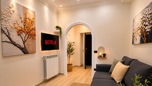 Una sala de estar moderna con un sofá negro, un televisor montado en la pared y un cuadro grande a la izquierda.