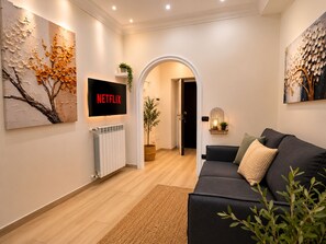 Ein modernes Wohnzimmer mit einer schwarzen Couch, einem an der Wand befestigten Fernseher und einem großen Gemälde links.