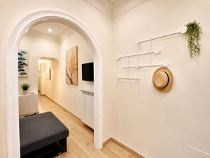 Ein Flur mit einer Bank, einem Heizkörper, einem Fernseher und einem an der Wand befestigten Haken für Hüte mit einer Pflanze.