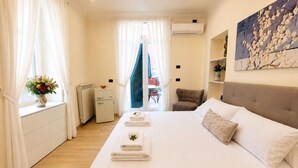 Habitación de hotel con cama, una silla, una mesita, un radiador y una ventana con cortinas.