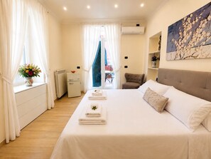 Ein Hotelzimmer mit Bett, Stuhl, kleinem Tisch, Heizkörper und einem Fenster mit Vorhängen.