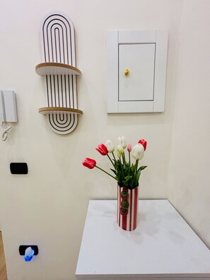 Eine weiße Wand mit einer Wandtafel, einem an der Wand befestigten Telefon und einem kleinen Tisch mit einer gestreiften Vasen voller Tulpen.