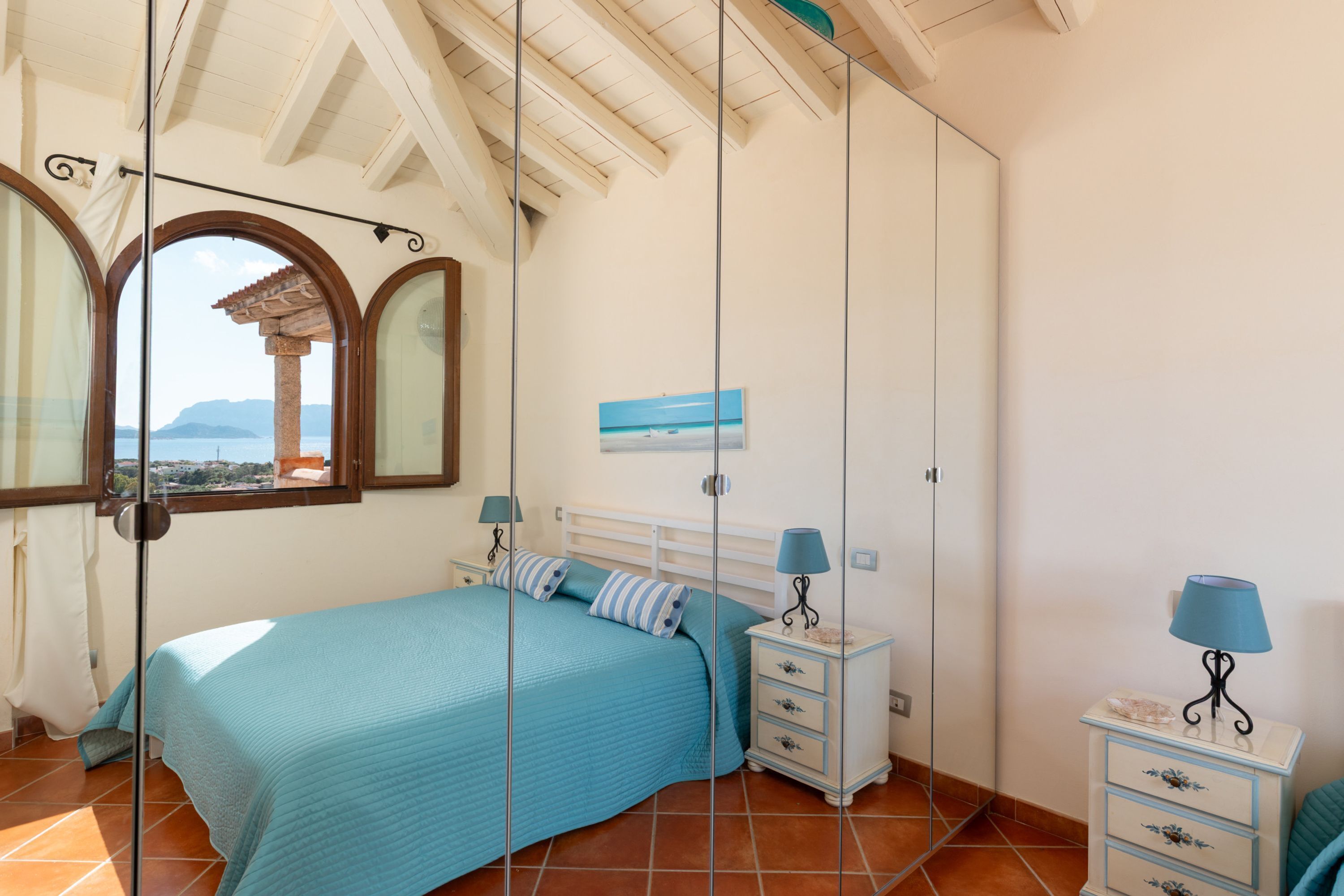 A bedroom with a bed, two bedside tables, a nightstand, a window with a view, and a wall-mounted painting.