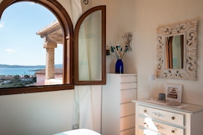 Ein Schlafzimmer mit Meerblick, einem großen Spiegel, einem Schminktisch und einer Vase mit Trockenpflanzen.