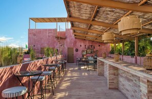 Eine Dachterrasse mit pinkfarbener Wand, Sitzgelegenheiten im Freien und einer Holzpergola.