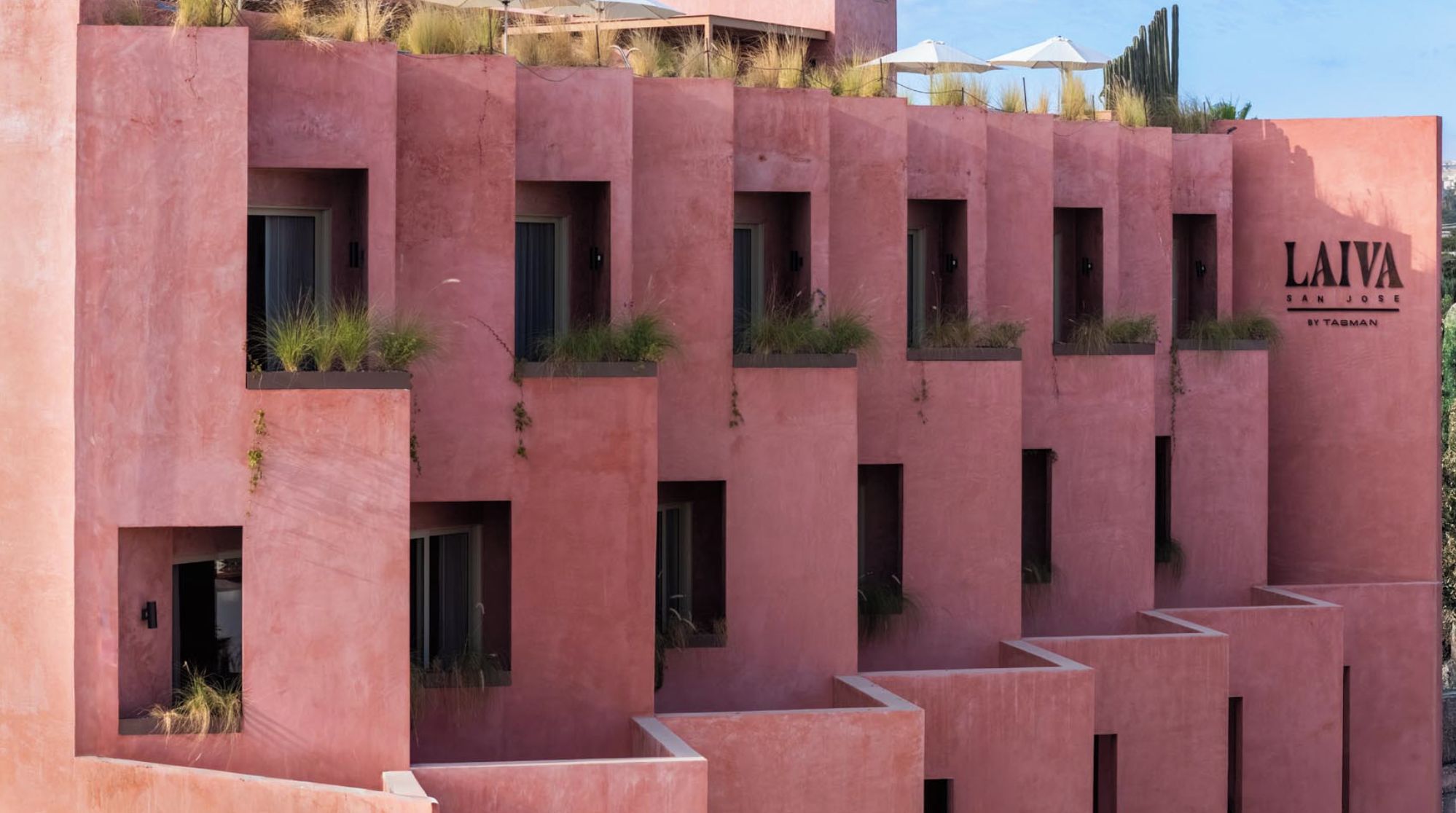 A building with a pink facade, multiple windows, and a sign that reads 'LAIVA SAN JOSE BY TAGMAN'.