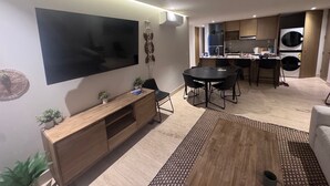 En moderne stue med et fladskærms-tv, et træunderholdningsmøbel, et spisebord med stole, et køkken med vaskemaskine og et gulvtæppe med mønster.