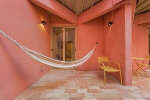 Un hamac est suspendu entre deux murs dans une pièce dont le sol est carrelé et où se trouve une chaise jaune.