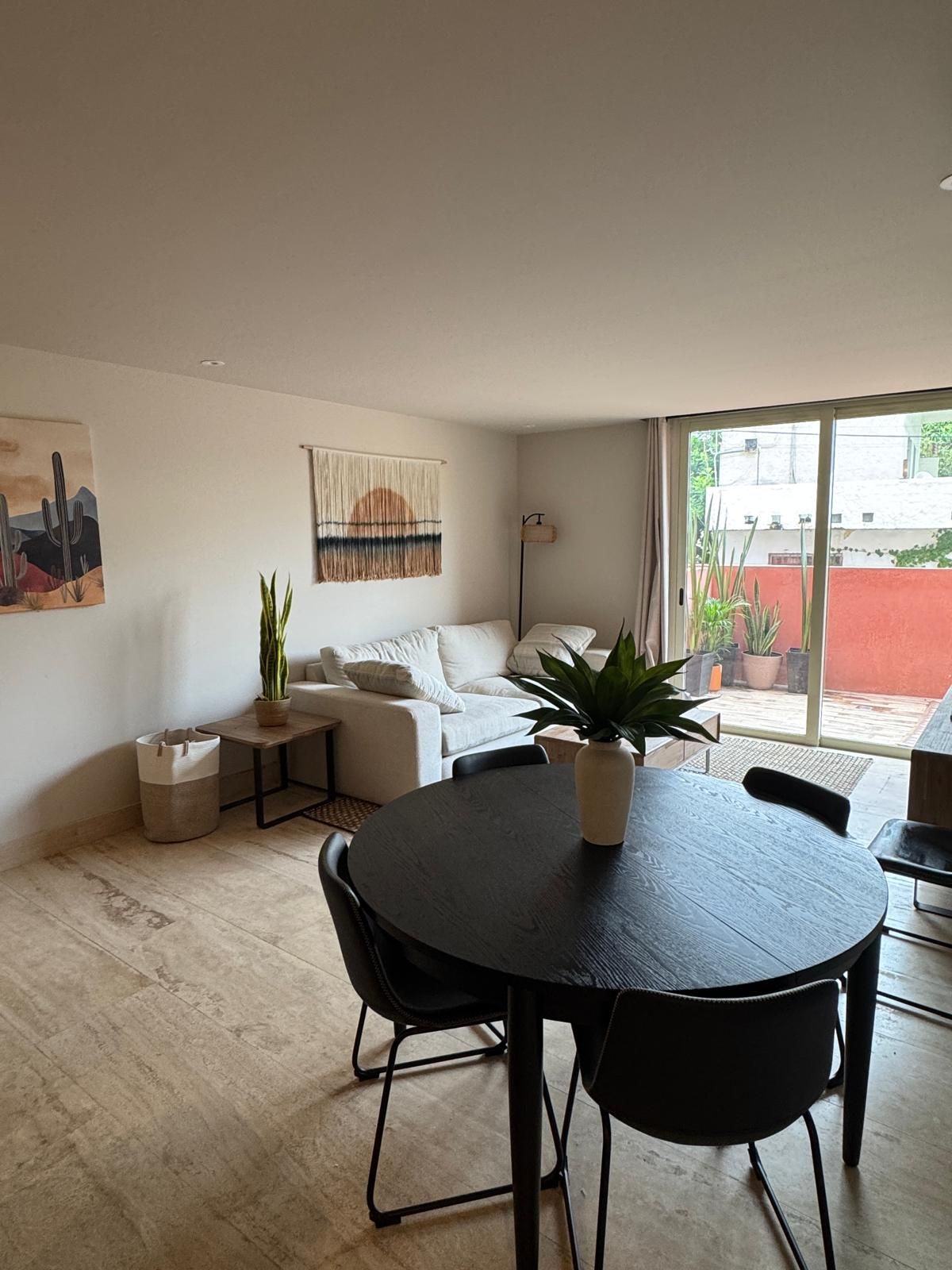 Un espacio de estar moderno con una mesa de comedor redonda, un sofá y una planta en maceta.