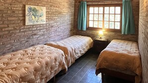 Una habitación con dos camas, una pared de ladrillo, techo de madera, una ventana con cortinas y un cuadro en la pared.
