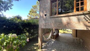 A brick building with a stone patio, a hammock, and a grill area.