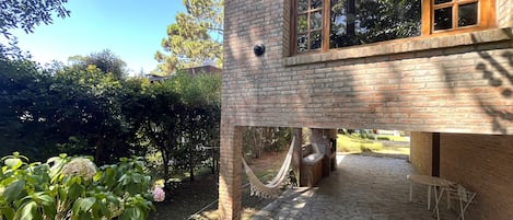 A brick building with a stone patio, a hammock, and a grill area.