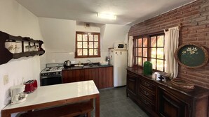 Une cuisine compacte équipée d’une cuisinière à gaz, d’un four à micro-ondes et d’un réfrigérateur. On y trouve une fenêtre avec des rideaux, un meuble en bois et une petite table avec un grille-pain.