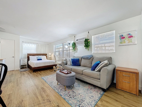 A bedroom with a bed, bedside table, chair, and a grey sofa. - Cozy studio in fantastic Dunedin with refreshing AC (Dunedin)
