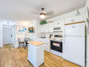 A compact kitchen with white cabinets, a microwave, a stove, a refrigerator, and a ceiling fan. - Cozy studio in fantastic Dunedin with refreshing AC (Dunedin)