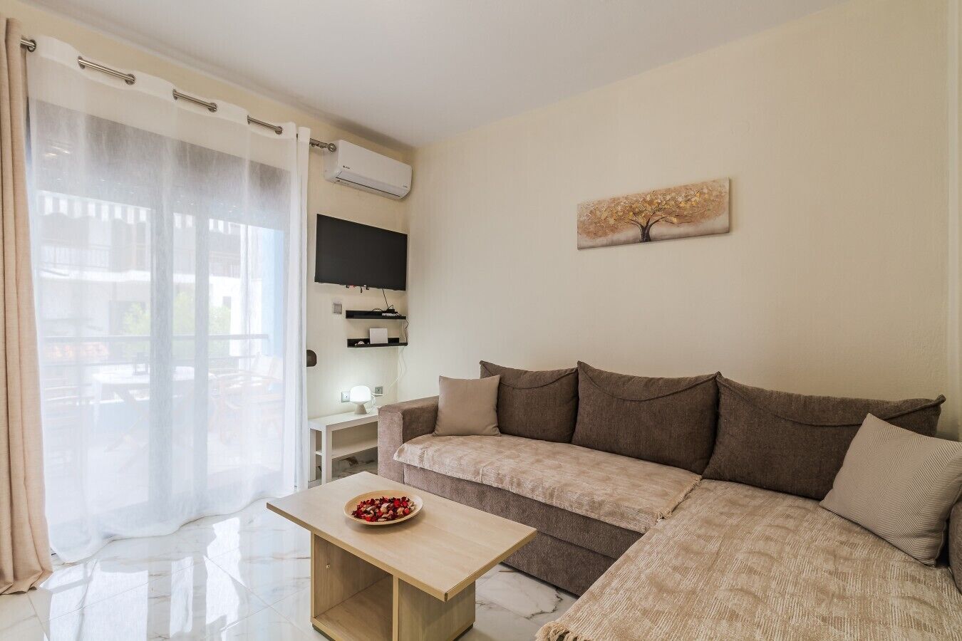 Uma sala de estar com um sofá, uma mesinha, uma televisão e um quadro na parede.