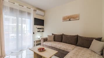 Uma sala de estar com um sofá, uma mesinha, uma televisão e um quadro na parede.