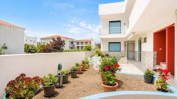 Um edifício residencial moderno com área de pátio, plantas em vasos e mobiliário de exterior.