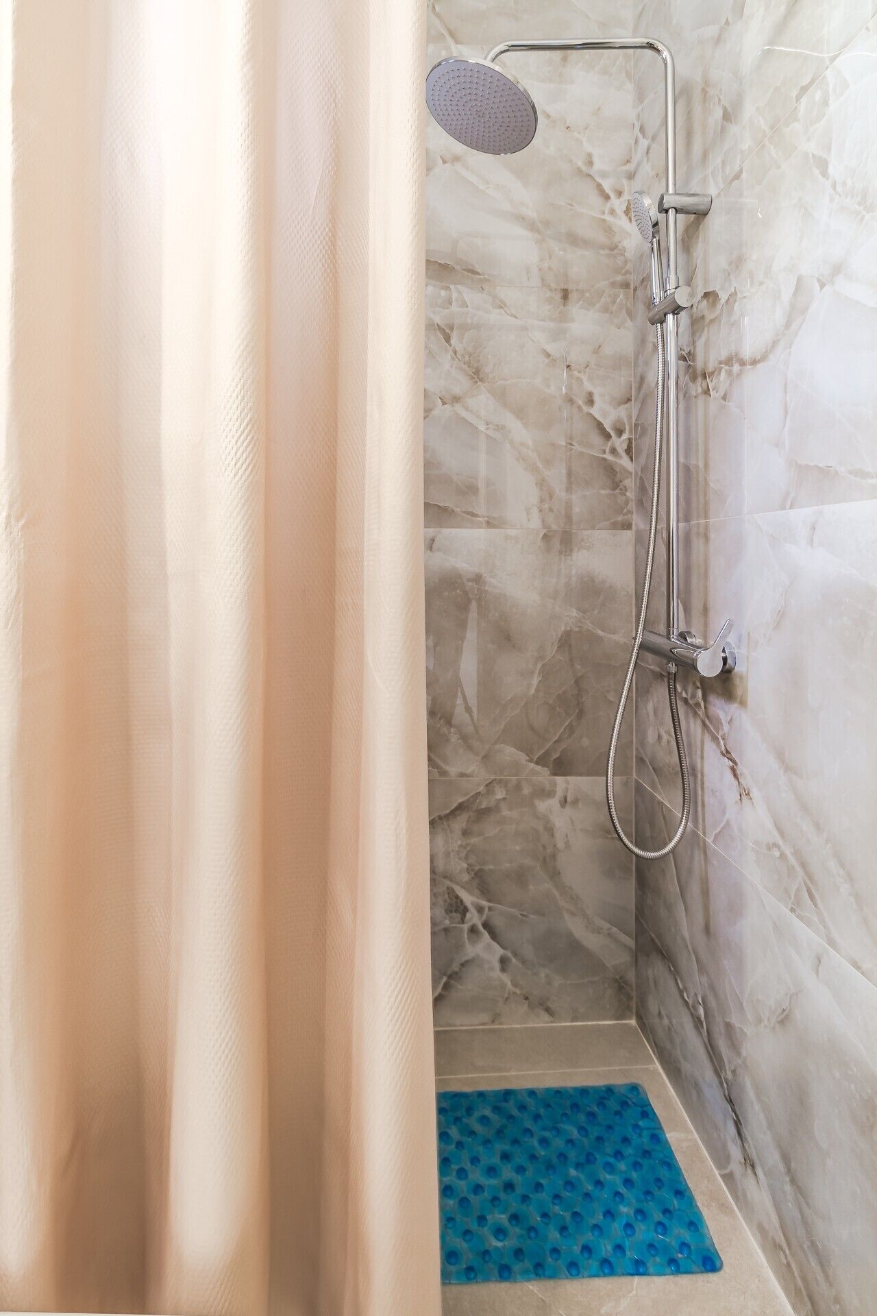 A shower with a handheld showerhead and a handheld shower attachment, a blue non-slip mat, and a marble wall.