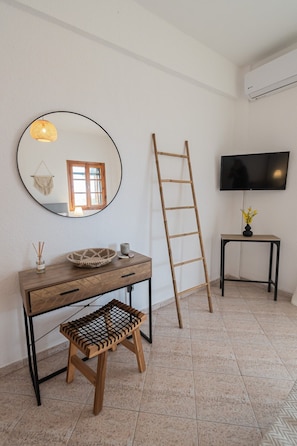 Quarto com escrivaninha de madeira, espelho, televisão, escada e pequena mesa com um vaso.