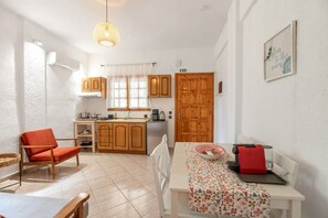Une cuisine de taille réduite avec des meubles en bois, une table à manger recouverte d’une nappe à motifs et une chaise rouge.