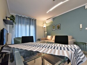 A modern hotel room with a glass dining table, a sofa, a TV, and a lamp. - Serenity Apartment by RentalsPro - Nea Moudania (Nea Moudania)