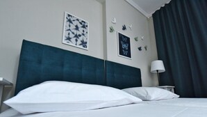 Un letto rifatto con lenzuola bianche, una testiera blu scuro e una parete decorata con farfalle.