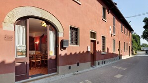 A building with a large arched entrance, a dining area with chairs and a table, and a sign indicating a tourist location. - Casa del Custode: Via degli Dei – Mugello Circuit (Tagliaferro)