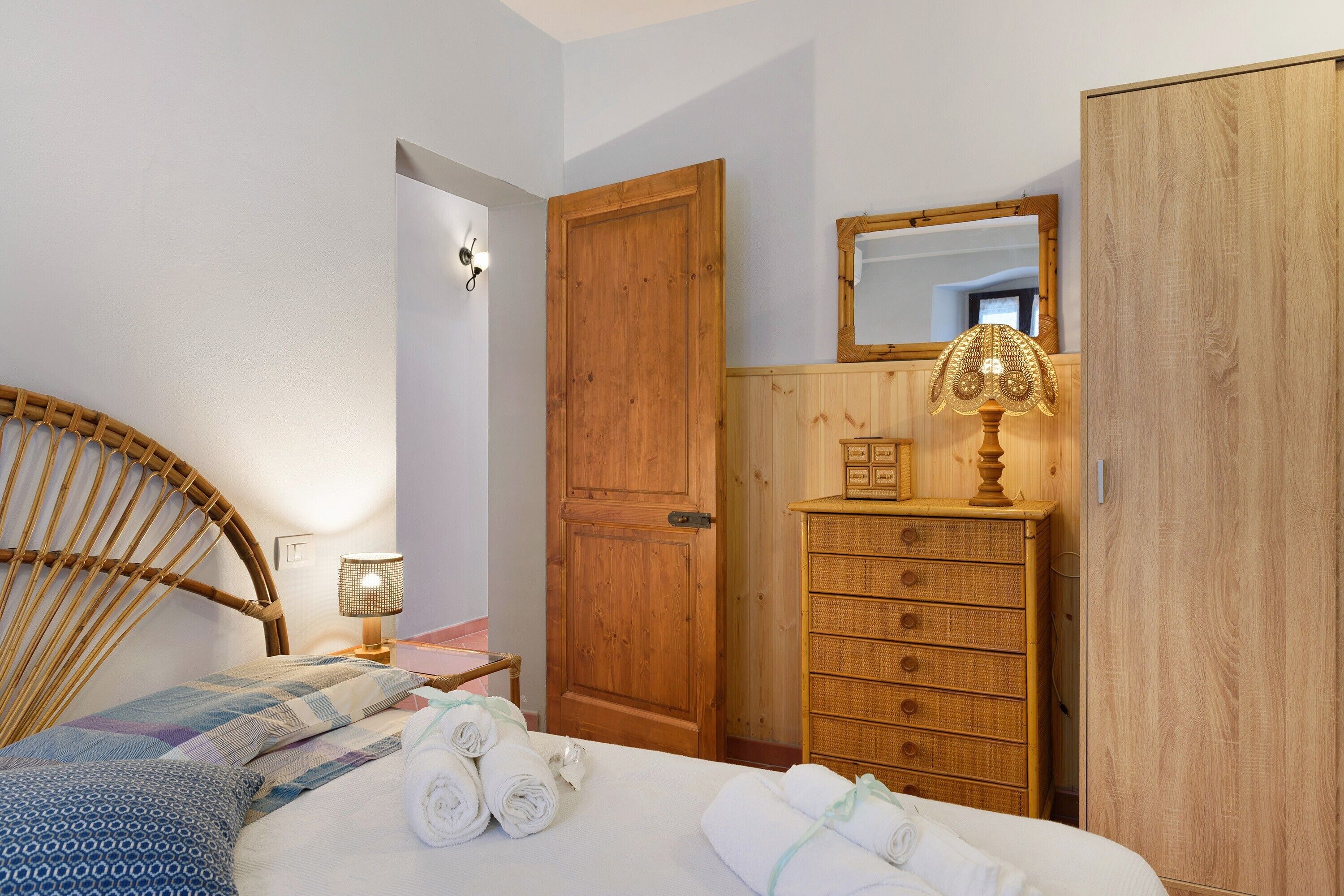 A bedroom with a bed, a wooden wardrobe, a dresser, a mirror, and a lamp.
