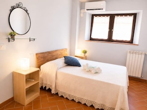 A bedroom with a bed, bedside table, lamp, window, air conditioning unit, and radiator.