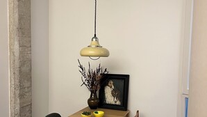 Een eetgedeelte met een houten tafel, twee stoelen, een hanglamp, een vaas met gedroogde planten en een lijst met een afbeelding.