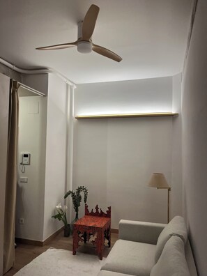 Een kamer met plafondventilator, een klein tafeltje met een vaas, een bank en een lamp.