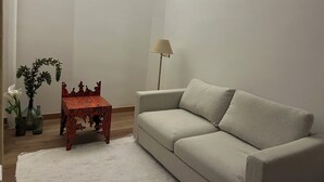 Een woonkamer met een bank, een klein houten tafeltje, een vloerlamp en een witte vloerkleed.