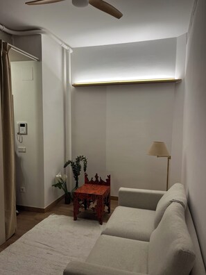 Una sala de estar con un sofá, una mesita con una planta, una lámpara de pie y un ventilador de techo.