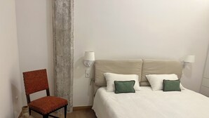 Een slaapkamer met een bed, twee kussens, een stoel, een wandlamp en een vaas.